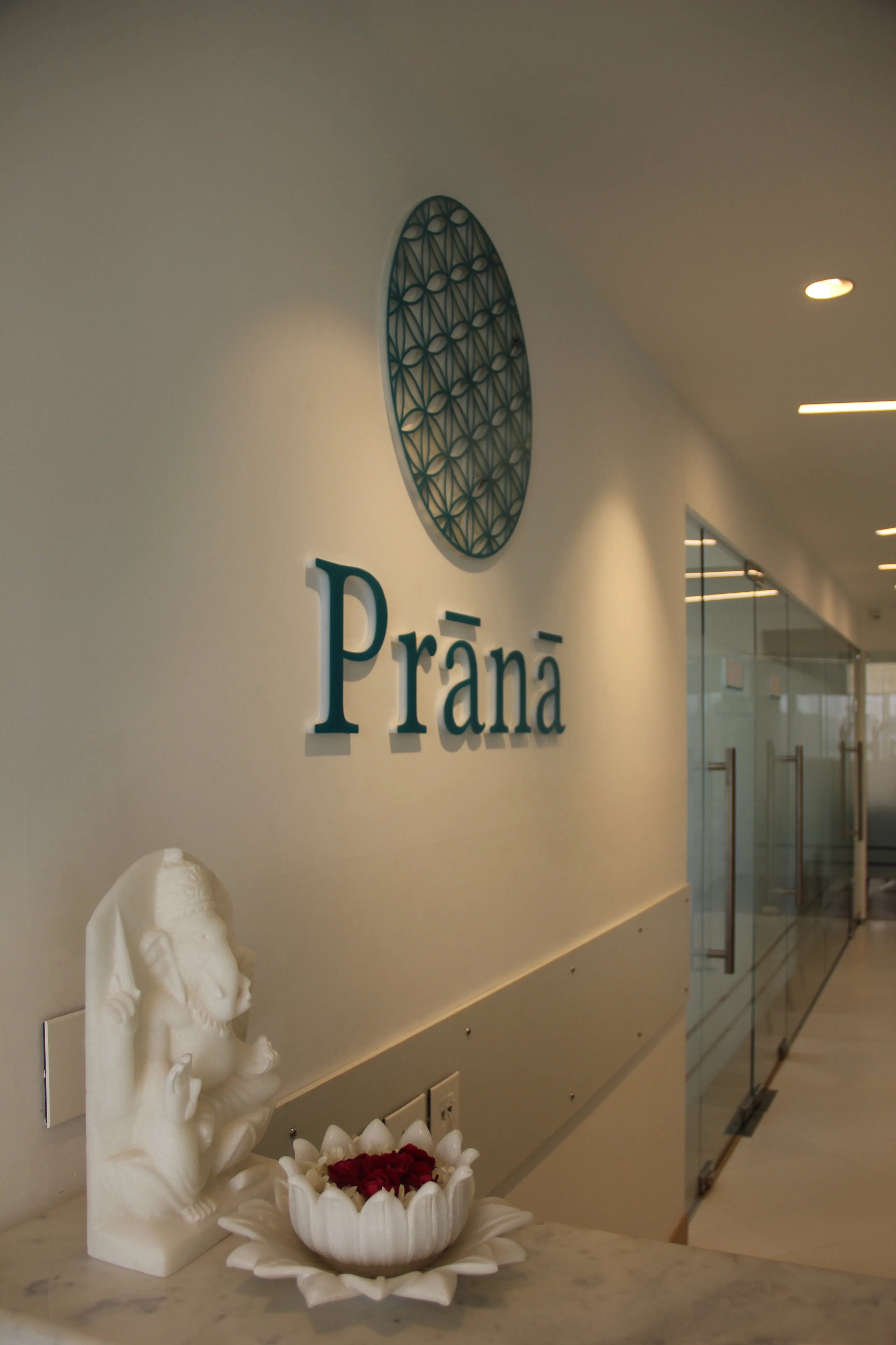 Prana reception wall with the center's wordmark, lotus flowers, and a Ganesha sculpture